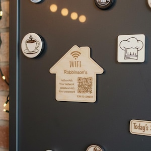 Könnte beinhalten: Holz-WiFi-Schild in Form eines Hauses mit dem Text "WIFI Robinson's" und einem QR-Code. Weitere Magnete sind eine Kaffeetasse, eine Kochmütze und ein Schild "Today's Specials", alles auf einer dunkelgrauen Oberfläche.