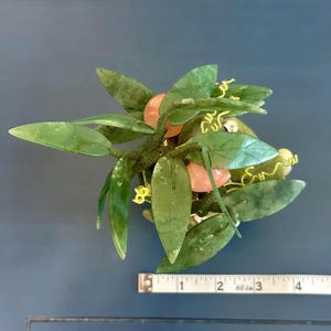May include: A decorative jade plant sculpture with green leaves and pink fruit. The sculpture is approximately 4 inches long, with a measuring tape in the image for scale. The leaves have a glossy finish.