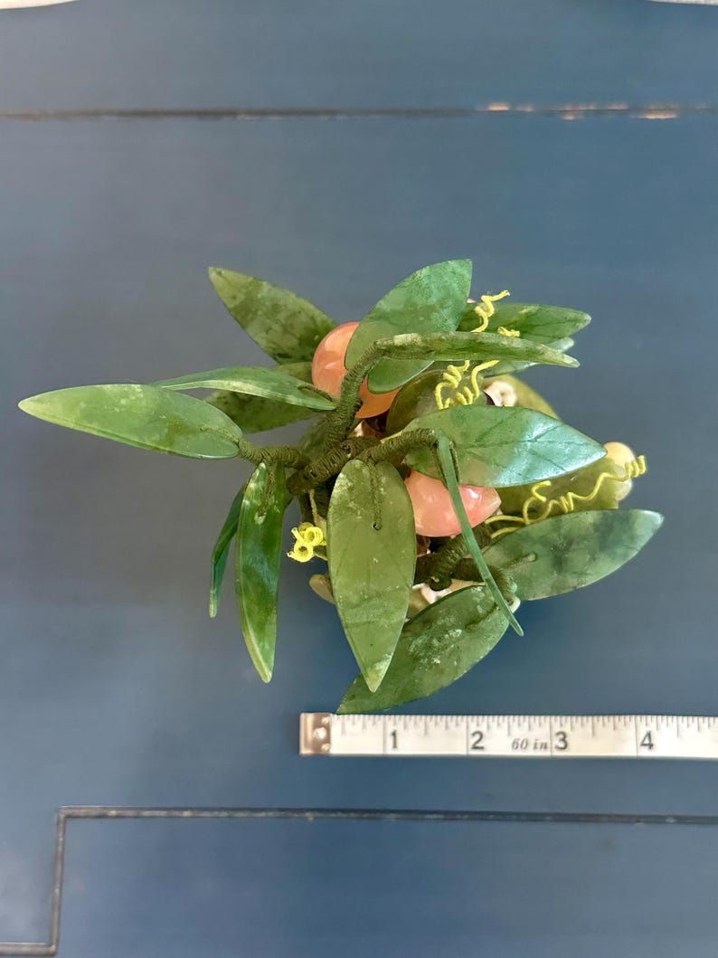 May include: A decorative jade plant sculpture with green leaves and pink fruit. The sculpture is approximately 4 inches long, with a measuring tape in the image for scale. The leaves have a glossy finish.