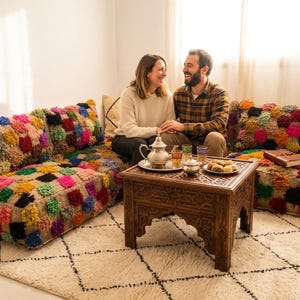 May include: A low-profile modular floor sofa upholstered in a natural tan fabric featuring a vibrant, multi-colored tufted square pattern. The set includes matching back cushions and is paired with a dark brown carved wooden side table.