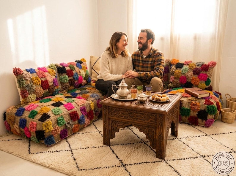 May include: A low-profile modular floor sofa upholstered in a natural tan fabric featuring a vibrant, multi-colored tufted square pattern. The set includes matching back cushions and is paired with a dark brown carved wooden side table.