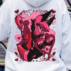 May include: White hoodie featuring a vibrant graphic on the back. The design showcases a pink and red cartoon character with heart and skull motifs. The hoodie has a drawstring hood and long sleeves, perfect for casual wear.