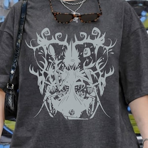May include: Dark grey t-shirt with a large, light grey graphic design. The design appears to be an abstract illustration. The text "PEPPER COMFORT COLORS" is printed at the top left of the image. The shirt is worn with grey jeans.
