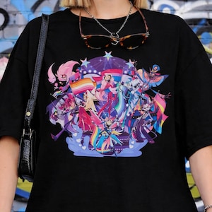 May include: Black t-shirt featuring a colorful graphic design with multiple figures, rainbows, and flags. The design includes various characters in vibrant colors. The shirt is a casual, oversized style.