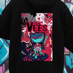 May include: Black hoodie featuring a colorful graphic of a character from "Hazbin Hotel" with the text "The Vees". The design includes red, blue, and white elements. The hoodie is made of a soft material.