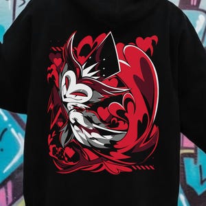 May include: Black hoodie featuring a vibrant graphic on the back. The design showcases a stylized character in red, white, and black, set against a backdrop of red heart shapes. The hoodie has a hood and long sleeves.