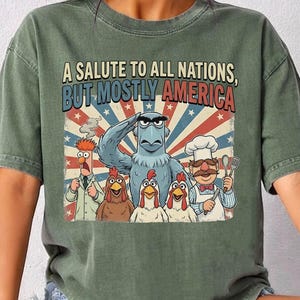 May include: Green t-shirt with the text "A Salute to All Nations, But Mostly America." The graphic features cartoon characters, including an eagle saluting, chickens, and a chef. The shirt is labeled "MOSS COMFORT COLORS."