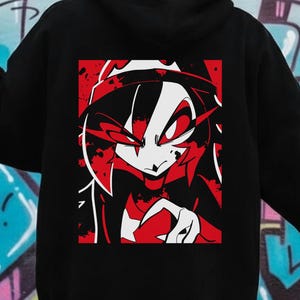 May include: Black hooded sweatshirt featuring a red, white, and black graphic design on the back. The graphic is a stylized anime-style character with red accents. The sweatshirt has a drawstring hood and long sleeves.