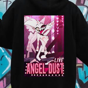 May include: Black hoodie featuring a colorful graphic of a cartoon character with the text "LIVE ANGEL DUST". The graphic is in a rectangular shape and is centered on the back of the hoodie. The hoodie has a hood and long sleeves.