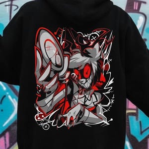 May include: Black hoodie featuring a red, white, and gray graphic of a cartoon character with sharp teeth and red eyes. The design is on the back of the hoodie, set against a graffiti background.