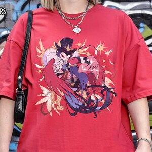 May include: Red t-shirt with a graphic design featuring two cartoon characters embracing, with text that reads "RED COMFORT COLORS". The shirt is a short-sleeved, oversized style.