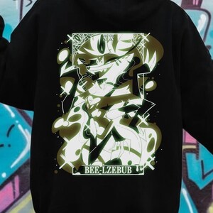 May include: Black hoodie with a graphic design on the back. The design features a stylized illustration with the text "BEE-LZEBUB" at the bottom. The hoodie is shown against a graffiti background.
