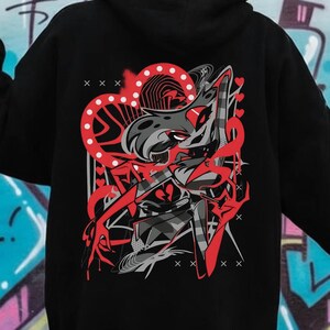 May include: Black hoodie with a graphic design on the back featuring a red and gray cartoon character with a heart-shaped design. The hoodie has a hood and long sleeves. The background is a colorful graffiti wall.