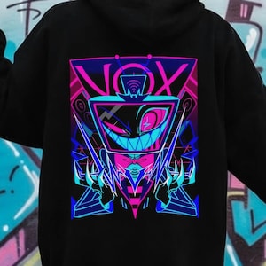 May include: Black hoodie with a vibrant graphic on the back featuring the word "NOX" and a stylized character in neon pink, blue, and purple. The design has sharp angles and a futuristic aesthetic. The hoodie is set against a graffiti background.