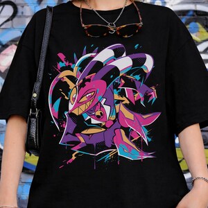 May include: Black t-shirt featuring a colorful cartoon character design. The graphic includes shades of purple, pink, and teal, with a stylized, expressive face. The shirt is a casual, oversized fit.