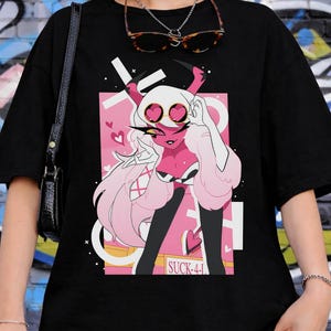 May include: Black t-shirt featuring a pink and white cartoon character with heart-shaped eyes, horns, and long white hair. The graphic is set against a pink background with the text "SUCK-41". The shirt is worn by a person.