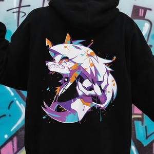 May include: Black hoodie featuring a colorful wolf graphic on the back. The wolf design incorporates shades of white, purple, orange, and blue. The hoodie has a hood and long sleeves, suitable for casual wear.