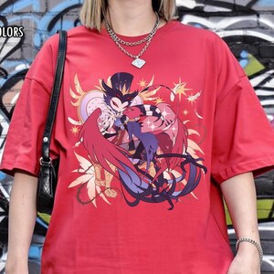 May include: Red t-shirt with a graphic design featuring two cartoon characters in a loving embrace, with the text "RED COMFORT COLORS" in the upper left corner. The shirt is worn with gray jeans and a black shoulder bag.