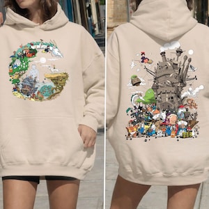 May include: Sand-coloured hoodie with a colourful graphic on the front and back. The front graphic depicts a circular scene with a dragon and other characters. The back graphic shows a castle and various animated characters. The hoodie has a hood and a front pocket.