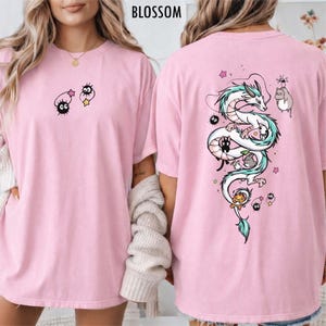 Pode incluir: T-shirts rosa com design de desenho animado. Uma camisa apresenta um drag&atilde;o com um design turquesa e branco nas costas. A outra camisa tem um design de desenho animado na frente. A palavra "BLOSSOM" &eacute; impressa no topo.