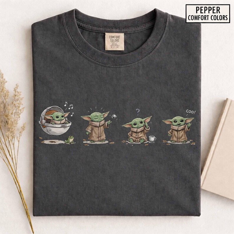May include: Dark gray t-shirt featuring a cartoon character in various poses. The character is green with large ears and wears a brown cloak. The shirt has the text "Pepper Comfort Colors" in a white rectangle.