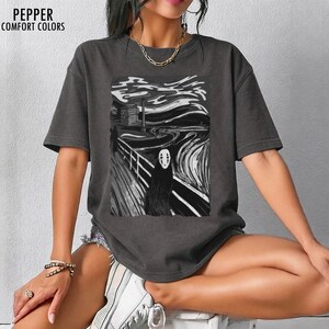 Op de afbeelding: Donkergrijs t-shirt met een zwart-witte afbeelding van een personage uit Spirited Away in de stijl van De Schreeuw. De tekst "PEPPER COMFORT COLORS" staat linksboven.