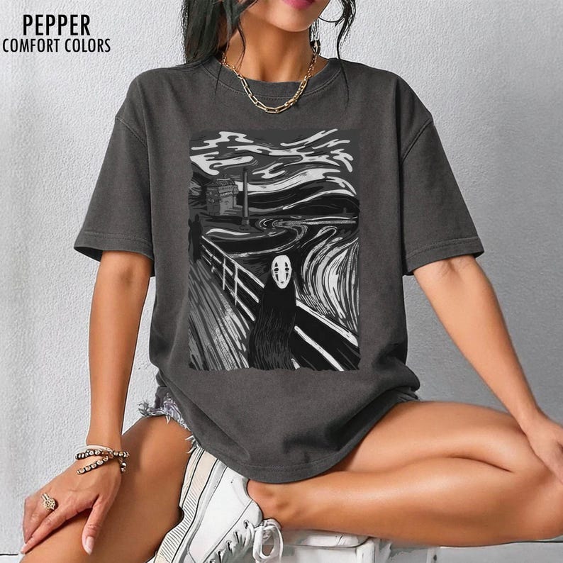 Op de afbeelding: Donkergrijs t-shirt met een zwart-witte afbeelding van een personage uit Spirited Away in de stijl van De Schreeuw. De tekst "PEPPER COMFORT COLORS" staat linksboven.