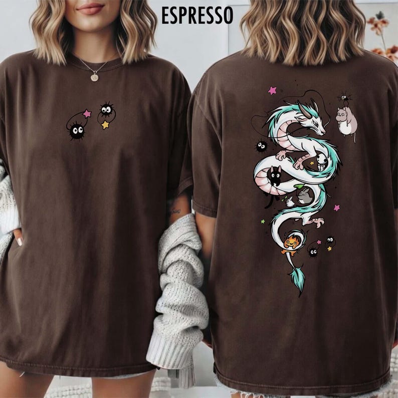 Pode incluir: Camiseta cor de caf&eacute; com um design fantasioso. A frente exibe dois personagens de desenho animado com estrelas. A parte de tr&aacute;s mostra um drag&atilde;o branco com detalhes em verde-azulado, cercado por outros personagens e estrelas. A camisa tem um caimento folgado.