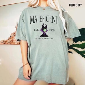 May include: A light green t-shirt with the word "Maleficent" and a graphic of the Disney villain. The design includes "Est. 1959" and "Disney Villains". The shirt has a loose fit.