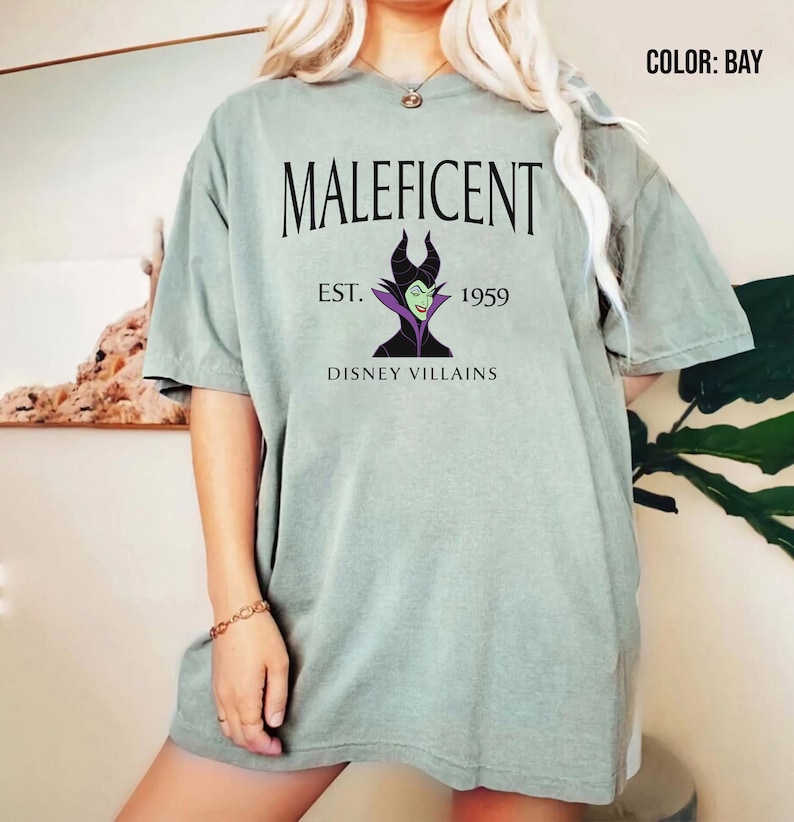 May include: A light green t-shirt with the word "Maleficent" and a graphic of the Disney villain. The design includes "Est. 1959" and "Disney Villains". The shirt has a loose fit.