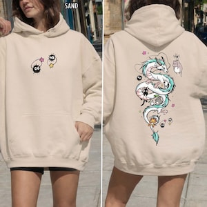 Pode incluir: Moletom cor de areia com bolso frontal e capuz. A frente exibe personagens de desenhos animados, enquanto a parte de tr&aacute;s mostra um desenho de drag&atilde;o branco e turquesa com personagens de desenhos animados adicionais. A palavra "SAND" &eacute; vis&iacute;vel no topo.