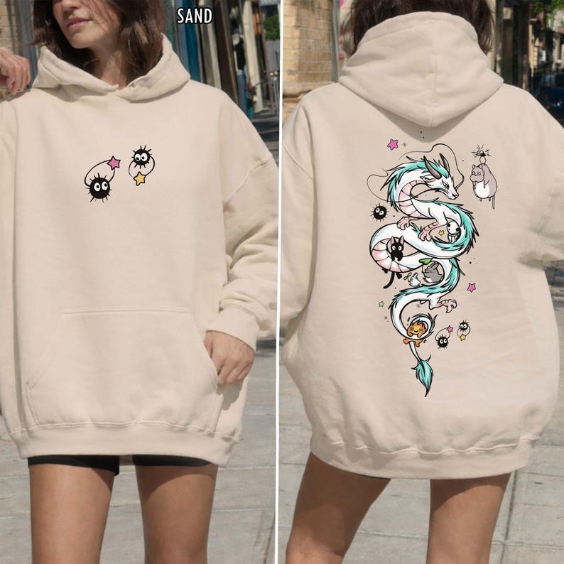 Pode incluir: Moletom cor de areia com bolso frontal e capuz. A frente exibe personagens de desenhos animados, enquanto a parte de tr&aacute;s mostra um desenho de drag&atilde;o branco e turquesa com personagens de desenhos animados adicionais. A palavra "SAND" &eacute; vis&iacute;vel no topo.
