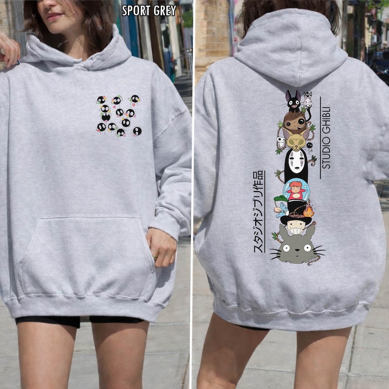 May include: Sport grey hoodie featuring a front pocket and a hood. The front displays a pattern of black and white cartoon characters. The back showcases a vertical stack of Studio Ghibli characters with Japanese text.
