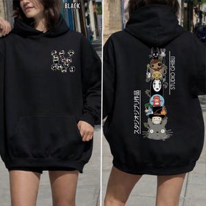 May include: Black hoodie featuring a front pocket and a hood. The front displays a cluster of cartoon characters. The back showcases a vertical stack of Studio Ghibli characters with Japanese text and the words "STUDIO GHIBLI".