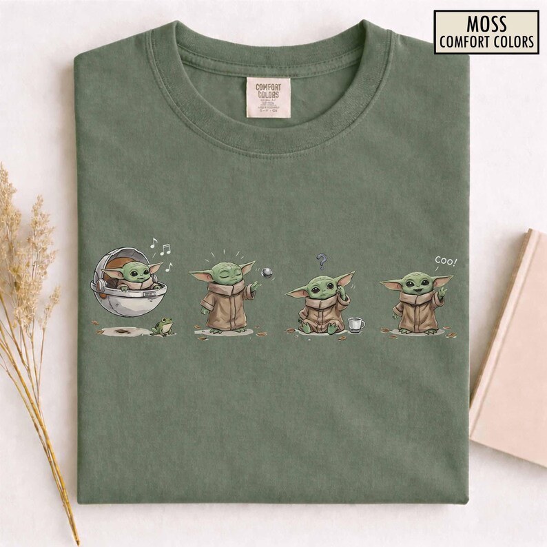 May include: Moss green t-shirt with a graphic of a character in different poses. The character is in a pod, playing with a ball, confused, and saying "coo!". The shirt has the text "MOSS COMFORT COLORS".