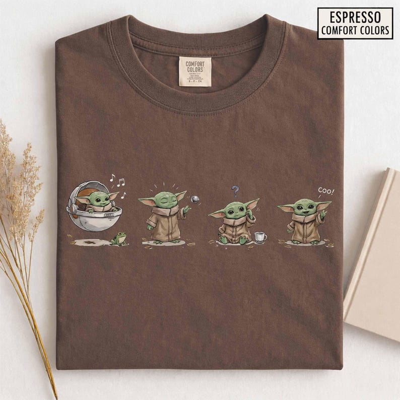 May include: Espresso-colored t-shirt featuring a cartoon depiction of a green alien character in various poses. The graphic includes the text "Espresso Comfort Colors" and the character is shown with a frog, a ball, and a cup.