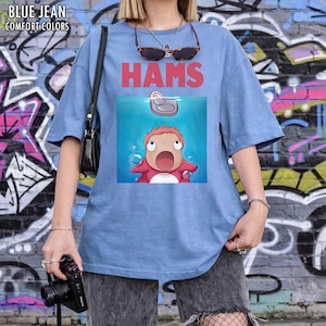 May include: A pale blue t-shirt with the word "HAMS" in red. The shirt has a cartoon graphic of a character in a blue water scene. The words "BLUE JEAN COMFORT COLORS" are printed at the top left.
