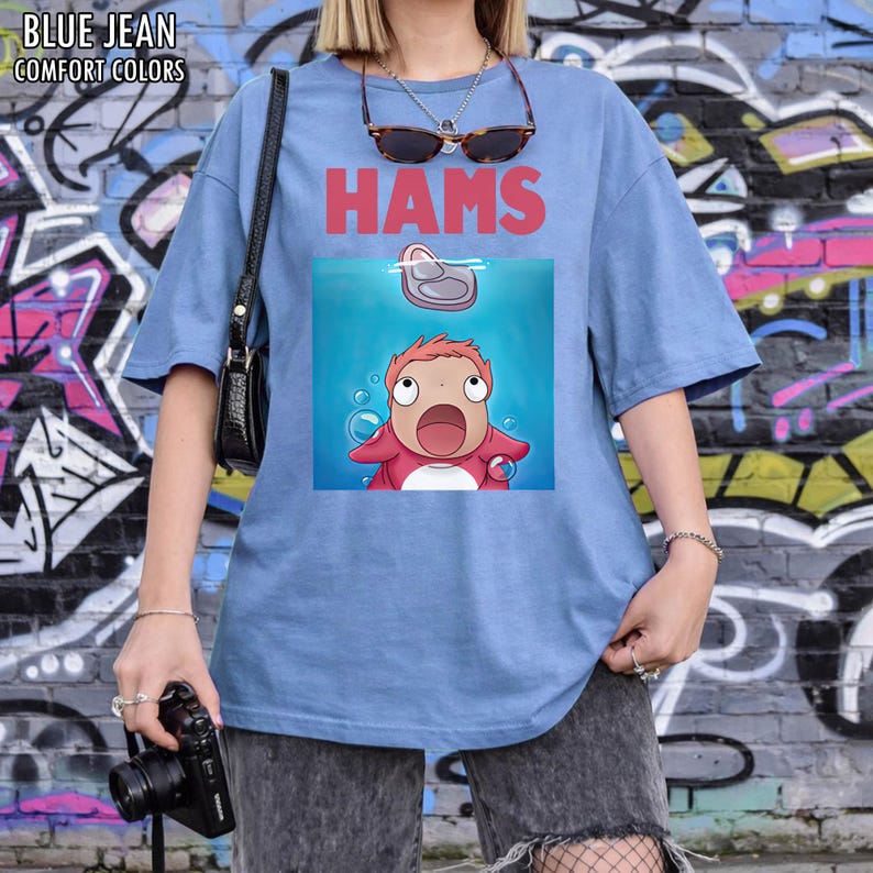 May include: A pale blue t-shirt with the word "HAMS" in red. The shirt has a cartoon graphic of a character in a blue water scene. The words "BLUE JEAN COMFORT COLORS" are printed at the top left.