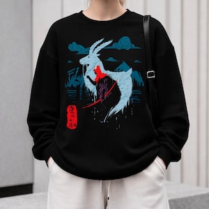 Peut inclure: Sweat-shirt noir avec un motif graphique d'une cr&eacute;ature ressemblant &agrave; une ch&egrave;vre bleu clair et une figure rouge, sur fond de nuages et de montagnes bleus. Texte japonais sur une &eacute;tiquette rouge. V&ecirc;tement d&eacute;contract&eacute;.