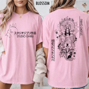 May include: Light pink t-shirts with black Studio Ghibli graphics. The front features a Totoro design with Japanese text and "Studio Ghibli." The back displays a detailed illustration of various Ghibli characters and text.