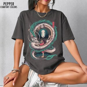 May include: Dark gray t-shirt featuring a Spirited Away graphic. The design includes a white dragon with teal accents, a girl in a red dress, and a character with a white mask. The text "Pepper Comfort Colors" is at the top left.