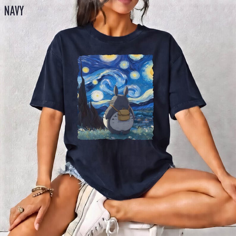 May include: Navy blue t-shirt featuring a graphic of Totoro from My Neighbor Totoro, set against a backdrop inspired by Van Gogh's "Starry Night." The image includes a gray Totoro with a backpack, and the text "NAVY" is in the upper left corner.