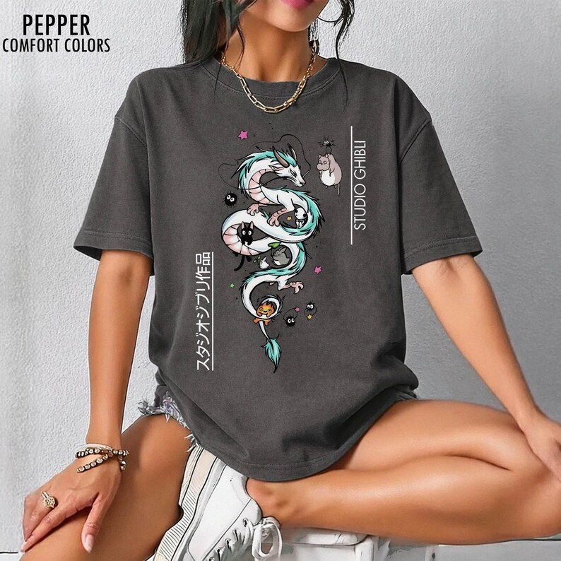 May include: Dark gray t-shirt featuring a white and teal dragon illustration with black cats and other characters. The text "STUDIO GHIBLI" and Japanese text are printed on the shirt. The shirt is from Pepper Comfort Colors.