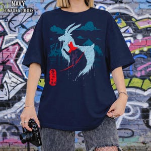 Peut inclure: T-shirt bleu marine avec un motif d'une cr&eacute;ature ressemblant &agrave; un cerf bleu clair avec des accents rouges et du texte japonais. Le t-shirt porte les mots "NAVY COMFORT COLORS" en haut. Le t-shirt est de coupe confortable.