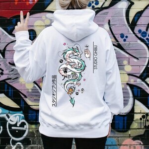 May include: White hoodie featuring a colorful illustration of a dragon and other characters, with the text "STUDIO GHIBLI" and Japanese text. The hoodie has a drawstring hood and long sleeves.