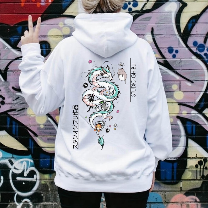 May include: White hoodie featuring a colorful illustration of a dragon and other characters, with the text "STUDIO GHIBLI" and Japanese text. The hoodie has a drawstring hood and long sleeves.