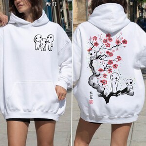 May include: White hoodie featuring a front pocket and a hood. The front displays a black graphic of three small figures. The back showcases a detailed illustration of a tree with red flowers and additional figures, with Japanese text.