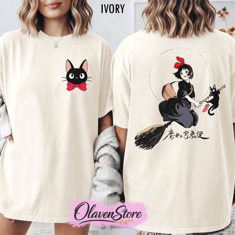 May include: Ivory-colored t-shirt featuring a black cat with a red bow tie on the front. The back of the shirt displays a cartoon illustration of a girl on a broom with a black cat, and Japanese text. The shirt has a crew neck.