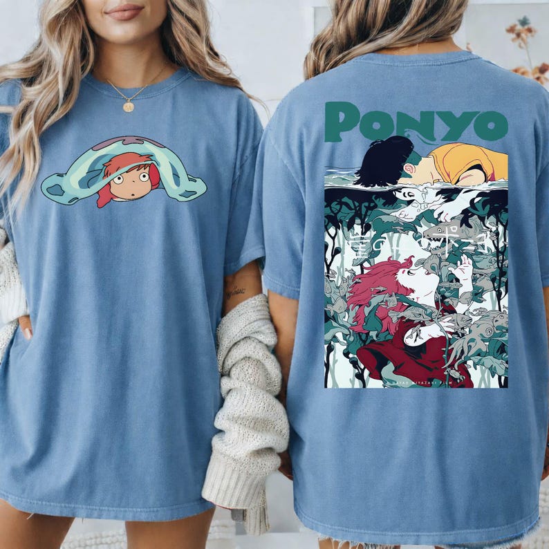 May include: Light blue t-shirts featuring the animated character Ponyo. One shirt displays Ponyo peeking out from under a blanket. The other shirt has the word "Ponyo" above an illustration of the character. The shirts are made of a soft material.