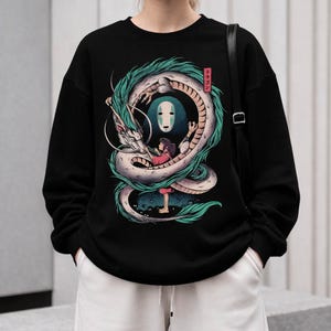 May include: Black sweatshirt featuring a detailed illustration of a white and teal dragon encircling a girl and a faceless spirit. The design includes Japanese text in a red box. The sweatshirt is worn by a person.